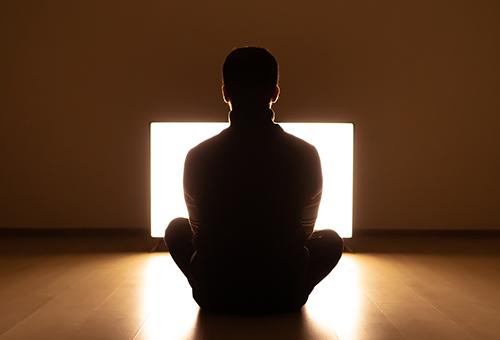 The male sitting on the floor in front of the television in the dark room