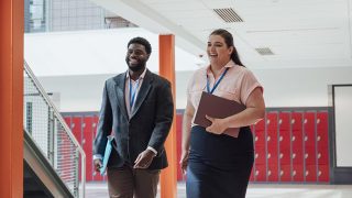 Two teachers walking through the school to their next class together while smiling and talking.